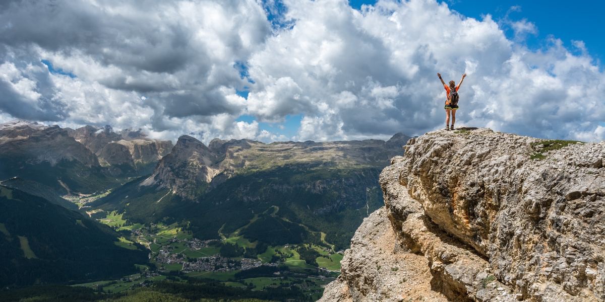 A hiker at the edge of a cliff with their arms up in the air